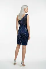 Vestido corto de un solo hombro, confeccionado en tul azul marino con forro interior. Presenta un diseño ajustado al cuerpo, decorado con lentejuelas y brillos distribuidos en un patrón floral sutil, con un borde de cuentas oscuras en el escote.