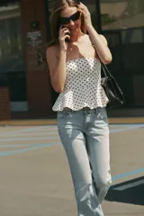 Top palabra de honor de color blanco con estampado de lunares negros, diseño sin tirantes y bajo con volados tipo peplum.