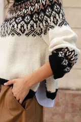Sweater de lana con diseño de jacquard en la parte superior, cuello redondo, mangas largas y puños acanalados. Presenta un corte holgado con tajos laterales y un diseño ligeramente más corto en la parte delantera.