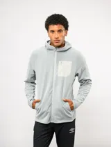 Campera de entrenamiento Umbro con capucha, cierre frontal completo y bolsillo en el pecho de nylon con cierre. Presenta una textura de tejido en relieve y logo de la marca estampado en el bolsillo.