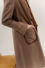 Tapado largo de corte recto y estilo minimalista, confeccionado en tela de color negro. Presenta solapas amplias, bolsillos frontales de parche y un diseño abierto que permite superponer capas.