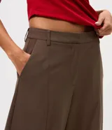 Pantalón de sastrería modelo barrel, color marrón, con tiro medio, cintura con pasantes, cierre frontal, bolsillos posteriores embutidos y recortes frontales estructurados.