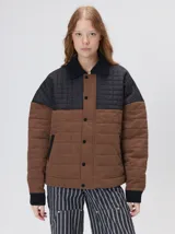 Campera acolchada de diseño bicolor en tonos marrón y negro. Presenta un estilo tipo bomber con cuello camisero de pana, cierre frontal oculto con botones a presión y bolsillos laterales. El canesú superior y los puños están confeccionados en pana, con detalles en gamuza, mientras que el cuerpo y las mangas poseen un acabado capitoné.