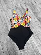 Malla entera plus size con diseño combinado, parte inferior negra y parte superior con estampado floral en tonos amarillos, rojos y celestes, con escote en V cruzado.