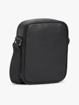 Morral de cuero sintético con acabado granulado color negro, de Tommy Hilfiger. Cuenta con un compartimento principal con cierre de cremallera, bolsillo frontal decorado con una franja tricolor vertical, correa cruzada ajustable y el logo metálico de la marca en la parte superior.
