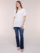 Blusa blanca de tejido de punto liviano con textura labrada en franjas verticales y caladas, de silueta evasé, con escote redondo, manga corta y ruedo asimétrico en picos.