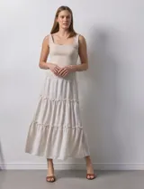 Falda larga de poliéster color beige con finas rayas verticales. Presenta una pretina ancha elastizada con efecto smock y volados en los ruedos de los tres paños que componen la falda.