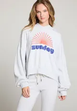 Hoodie gris jaspeado con capucha y mangas amplias. Estampado frontal con la palabra "Sunday" en azul y un sol naciente en naranja.