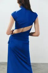 Vestido largo color azul, confeccionado en tejido elástico, con cuello alto, manga muy corta y detalle de lazada en la cintura. Cuenta con abertura en la espalda.