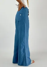 Pantalón de lino azul de corte palazzo, tiro alto y pierna ancha. Presenta costuras a la vista en color blanco y botón metálico.