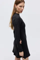 Vestido mini de manga larga confeccionado en punto fino, con cuello redondo y costuras decorativas frontales que definen la silueta. Presenta una falda con vuelo y pinzas en la espalda.