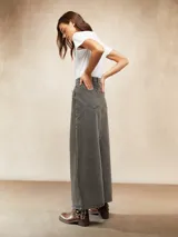 Falda larga de denim en color gris con efecto lavado, de corte recto y tiro alto. Presenta costuras verticales decorativas y cierre frontal con botón y cremallera.