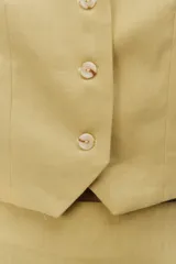 Chaleco sastrero de lino color amarillo, con escote en V, cierre frontal con botones y tiras ajustables con hebilla metálica en la espalda.
