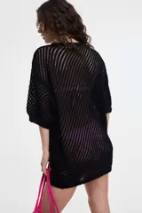 Vestido corto tejido color negro, con diseño calado en diagonal, cuello redondo y mangas cortas holgadas.