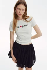 Remera de manga corta color blanco roto, con cuello redondo y estampado central con el texto "oui ❤ paris" en color negro y rojo.