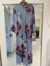 Vestido midi celeste con estampado floral en tonos fucsia y verde, cuello camisero, cierre frontal de botones y mangas largas.