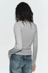 Chaqueta de punto color beige con escote en pico y manga larga, que incluye un top interior integrado con detalle de encaje a tono. Cierre frontal mediante botones.