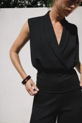 Top sin mangas confeccionado en tejido piqué, con escote cruzado tipo solapa y detalle de pliegues. Presenta una banda ancha ajustada en la cintura y un diseño de hombros caídos.