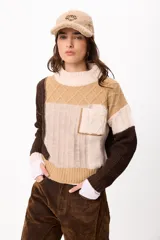 Sweater de punto con diseño patchwork en tonos tierra, crudo y marrón. Presenta cuello alto acanalado, bolsillo frontal tipo parche y mangas largas con puños acanalados.