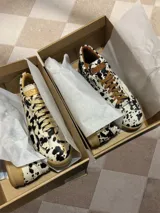 Zapatillas bajas con estampado animal print de vaca en blanco y negro, con cordones marrones y suela color caramelo.