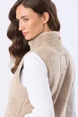 Chaleco de tejido sherpa color beige, con cuello alto y detalles en eco cuero. Diseño sin mangas que proporciona abrigo al torso manteniendo la libertad de movimiento.