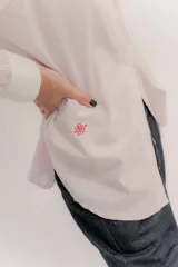 Camisa de manga larga color rosa claro con textura, cuello y puños blancos contrastantes. Los puños tienen tres botones rosados.