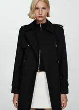 Trench coat negro de diseño recto y largo, con cuello de solapa, trabillas en los hombros y en las mangas, y cierre frontal con botones. Incluye bolsillos laterales y abertura posterior en el bajo.