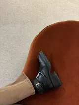 Botinetas de cuero negro con suela track, punta cuadrada y doble hebilla metálica decorativa en el lateral. Diseño de caña corta con cierre lateral.