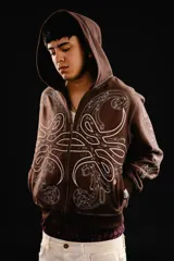 Hoodie con cierre frontal, color marrón, con diseño estampado de hojas de acanto en color blanco que recorre el frente y las mangas. Cuenta con bolsillos laterales y costuras visibles.