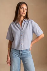 Camisa de manga corta con patrón de rayas verticales en tonos azul y blanco, cuello camisero y cierre frontal con botones.