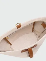 Cartera tipo bucket de tamaño pequeño, confeccionada en lona color crudo con detalles en cuero color tostado. Presenta una base redondeada, cierre de solapa con broche y correa ajustable para llevar al hombro.