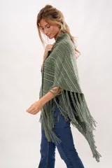 Ruana verde tejida en telar manual con lana merino. Presenta diseño con flecos y bolsillos de cuero natural.