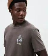 Remera de corte comfort color gris oscuro, con cuello redondo y mangas cortas. Presenta un pequeño estampado frontal con íconos étnicos y lettering en color blanco.