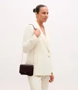 Cartera bandolera pequeña marca Satinato, confeccionada en poliuretano color bordó. Presenta una estructura rectangular con solapa frontal, cierre magnético y correa larga de cadena metálica dorada.