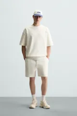 Bermuda de algodón color beige claro, corte relajado (relaxed fit), con cintura elástica ajustable mediante cordón y bolsillos laterales y trasero de plastrón.