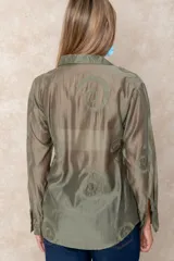 Camisa de manga larga en color blanco, confeccionada en tejido traslúcido con delicados bordados florales en hilo de seda al tono. Presenta cuello clásico, cierre frontal con botones y puños abotonados.