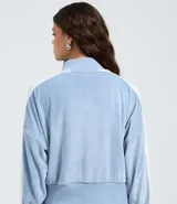 Suéter de plush color celeste con cuello alto, cierre frontal con cremallera y rayas laterales blancas en las mangas. Presenta puños y ruedo acanalados.