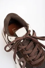 Zapatilla urbana de diseño robusto, confeccionada en una combinación de malla, gamuza y detalles en cuero sintético. Presenta una paleta de colores en tonos chocolate y crema, con suela dentada de goma de gran volumen.