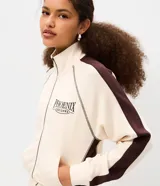 Campera deportiva de cuello alto con cierre frontal y bolsillos tipo canguro, en color beige con detalles marrones en las mangas y estampa localizada con texto "Phoenix Arizona".
