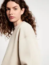 Buzo de cuello redondo en color beige, con diseño liso, mangas largas y puños y ruedo acanalados.