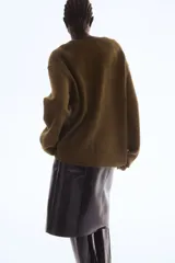 Sweater de punto suave color verde oliva, con cuello en V, hombros caídos y remates acanalados en puños y bajo.