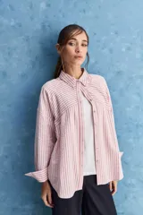 Camisa de calce relajado a rayas rosadas y blancas, con cuello camisero clásico y frente abotonado. Presenta recortes con cambio de dirección en las rayas y silueta amplia.