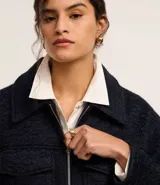 Campera corta azul marino de tejido boucle con cuello inglés, cierre frontal con cremallera y bolsillos grandes con solapa en el pecho.