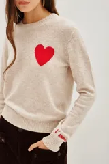 Sweater de punto color beige, con cuello redondo y manga larga. Presenta un corazón rojo bordado en el pecho y la palabra 'l'amour' bordada en el puño de la manga.