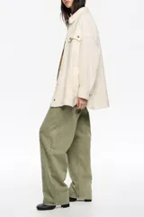 Sobrecamisa de corte oversize confeccionada en mezcla de lana, con cuello camisero, cierre frontal de botones y mangas largas con puños abullonados. Presenta bolsillos frontales con tapeta en el pecho y bolsillos laterales en el bajo, además de un detalle de pliegue en el canesú de la espalda.