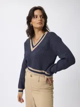 Sweater de punto con escote en V, diseño de estilo preppy en color azul marino con detalles de rayas en contraste color beige en el cuello, puños y ruedo. Presenta mangas largas y un corte ligeramente cropped.