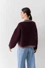 Cardigan de punto color bordó con cuello redondo, cierre frontal de botones y detalles de ribetes en contraste en cuello, puños y ruedo. Presenta un pequeño bordado de una raqueta de tenis en el pecho.