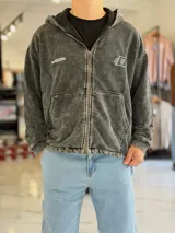 Campera tipo hoodie con cierre frontal y capucha, de corte boxy fit, efecto gastado acid wash en color gris, con bolsillos tipo canguro y pequeños estampados en el pecho.
