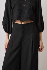 Pantalón largo negro de corte ancho y holgado, con bolsillos laterales y detalle de bordado calado en el ruedo.