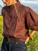 Camisa de lino color marrón oscuro con textura a rayas sutiles, cuello mao, cierre frontal con botones y mangas abullonadas tres cuartos.